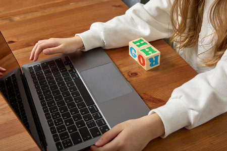 Close-up of a childs hands working on a laptop keyboard while sitting at a wooden table. Child is...