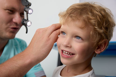 Otolaryngologist checks the hearing of a blond boy in a childrens hospital, uses a headlamp. Reception and consultation of an experienced ENT doctor of a little boy smiling during the examinationの写真素材