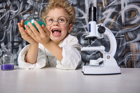 Little boy colored liquids under microscope overflowing with emotions joy and delight from process. In hands young scientist is test tube with ubstance which was obtained as result chemical reactionの写真素材