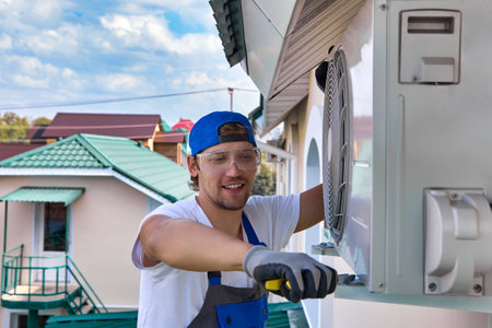 An experienced installer professionally twists the air conditioner mount on the wall outside the...