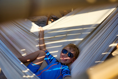 Happy little child is having fun on summer vacation, relaxing in a hammock. Beautiful funny little boy swinging in a hammock on the beachの写真素材