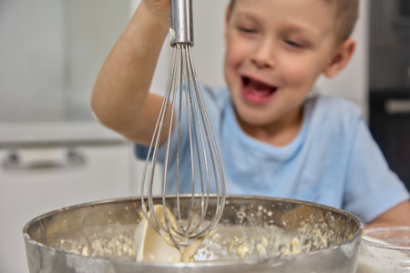 Close-up of a cheerful little boy kneading a liquid dough with a metal whisk in a large bowl. Young cute cook helps in the kitchen with the preparation of a pie for the holidayの写真素材