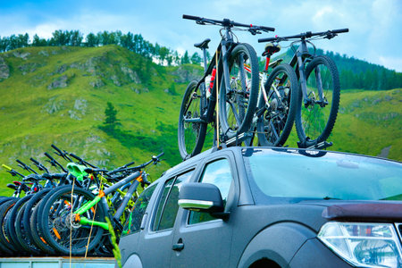 On the roof of the SUV are fixed for transportation several sports bicycles. On a trailer, a off-road vehicle carries fixed mountain bikes for touristsの写真素材