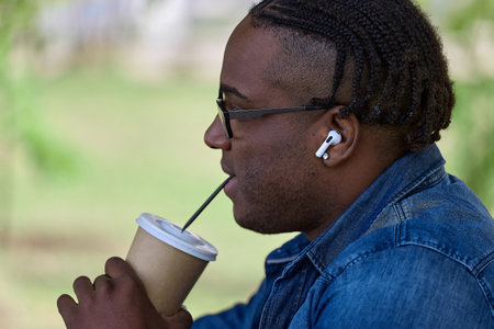An African student after exams in the park drinks coffee from their paper cup. Dark-skinned man with...