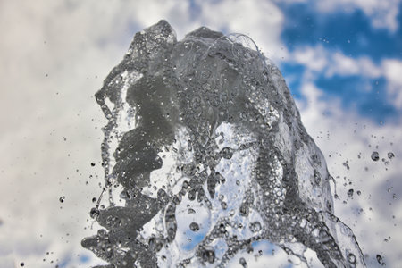 Splashes of pure transparent jet of water against the background of a blue sky with white clouds....