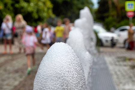 Children and adults walk next to the pedestrian city fountain, foam from the water close-up. Modern city fountain, a place of rest for citizens on a hot summer dayの写真素材