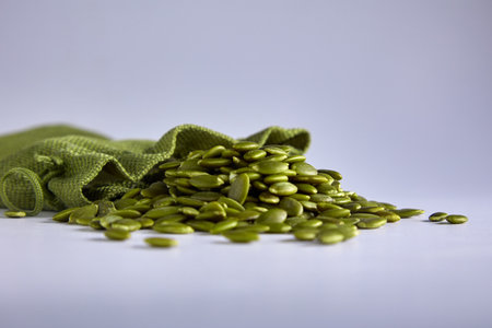 Peeled raw healthy pumpkin seeds are poured out of the green bag. Pumpkin seeds on a gray background in a storage bag. Healthy healthy food snackの写真素材