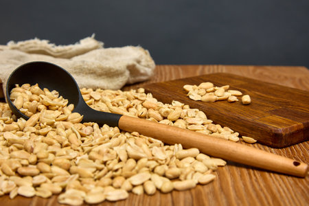 On a wooden table, scattered roasted peanuts are collected in a bag with a long cook. On a gray...
