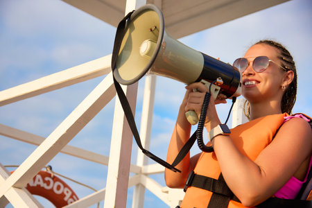 Pretty young girl in an orange life jacket talks to the loudspeaker about the sale. Happy bright young woman in sunglasses talking in a megaphone, announces a discount saleの写真素材
