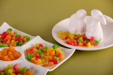 Delicious multi-colored candied fruit is laid out on a white curly dish on a yellow background. In a white porcelain plate with figures of hares, a dessert of sweet candied fruit is laid outの写真素材