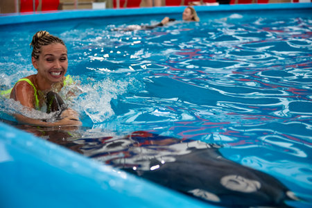 Smiling joyful woman bathes in the deep pool of the aquarium with a dolphin. Happy girl is engaged...