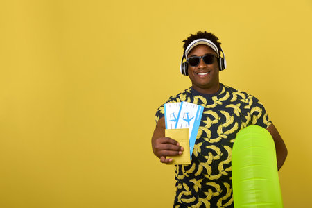 Sale of plane tickets by a tour operator. An African man cheerfully advertises airplane travel, shows a hundred tickets on a yellow backgroundの写真素材