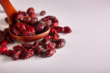 On a white background, a top view of a wooden spoon with large dry berries of healthy rosehip. Useful rosehip fruits are scattered on a white backgroundの写真素材