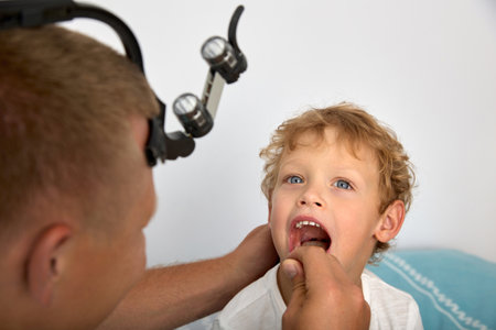 Experienced ENT doctor carefully examines palatine tonsils of child for presence of disease. Using a wooden spatula for the throat, the otolaryngologist checks the condition of the childs oral cavityの写真素材