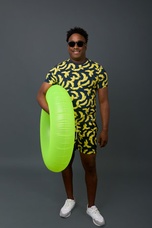 Tall, athletic African man with an inflatable circle poses on a gray background with a smile....