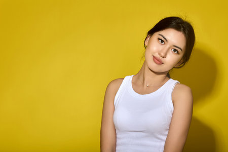 Close-up of Asian girl model looking at the camera on a yellow background, tilted her head. A foreign student in a white lane poses with a kind expression on her faceの写真素材