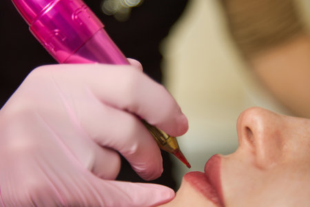 Close-up of the hand of a permanent makeup master in a pink latex glove with a typewriter. Performing lip tattooing for a young woman with a dense pink tone of lipstick effectの写真素材