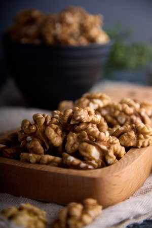 Large peeled walnuts are stacked on a wooden board. Delicious walnuts in a dark interior are...