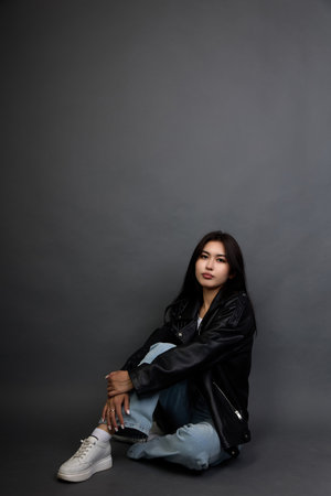 Cute brunette girl with a serious calm expression posing in a black jacket and jeans. Young woman...