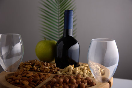Bottle of wine and two empty glass goblets on a walnut wooden stand on a gray background with a tropical leaf. Beautiful serving of nuts and white wine in a popular restaurantの写真素材