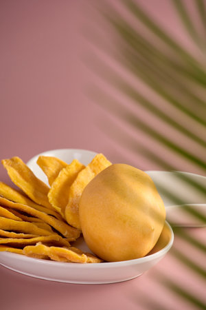 A whole mango and dried mango slices are laid out on a white plate. Mango can be seen through a...