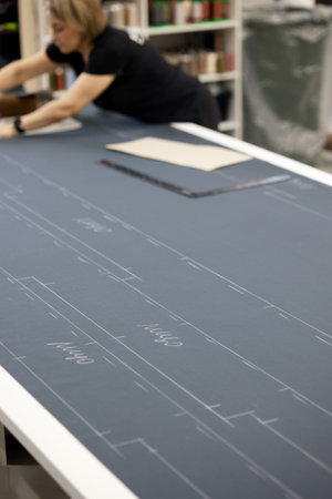 A woman dressmaker in a black t-shirt draws a straight line on the fabric, uses chalk and a ruler,...