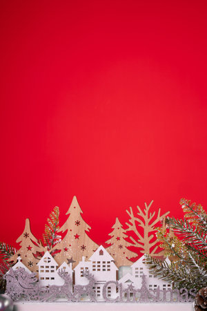 A charming collection of intricately crafted wooden Christmas village houses, surrounded by delightful bottle brush trees, all enhanced with sparkling silver glitter against a vibrant red background.の写真素材