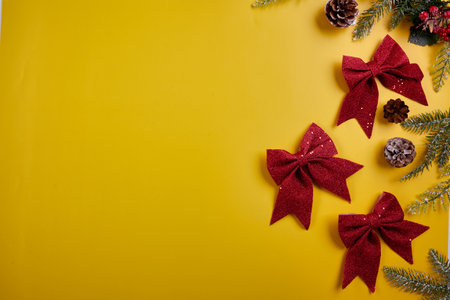 Three shiny red bows with pine cones on the right side of a solid yellow background. The image is suitable for Christmas or New Years cards, gift wrapping, website banners, and social media posts.の写真素材