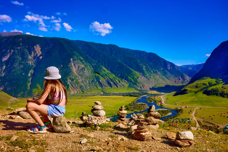 A serene moment unfolds as a young girl sits on a smooth pebble, absorbing the breathtaking view of...