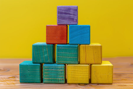 Growing Concept Multi-colored Wooden Blocks Form A Steady Pyramid Against Yellow Backdropの素材