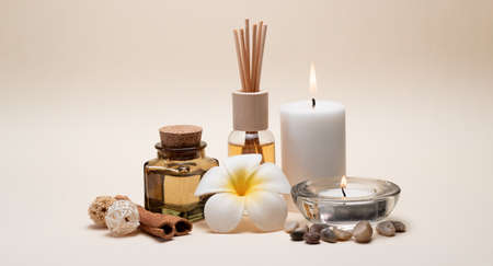 Beautiful spa composition with candles, frangipani flower, oil flasks and other decor elements.