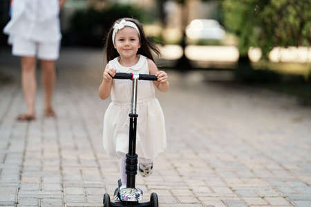 Happy cute little girl riding scooter outdoor