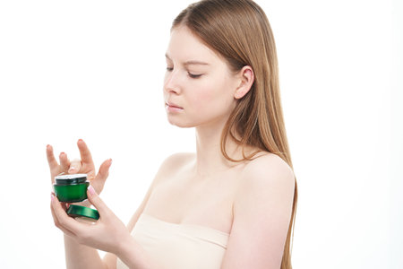 Redhead girl takes cosmetic cream out of jar on white background.の写真素材