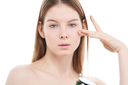 Girl applies cosmetic cream on her face on white background.