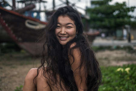 Portrait of smiling charming asian girl. Brunette with long curly hair posing. Looking at camera...