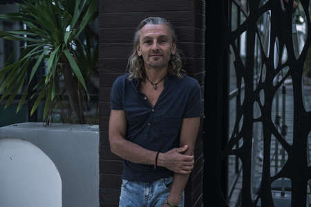 Tanned mature handsome man in t-shirt and jeans standing on the street. Long gray hair. Portrait....