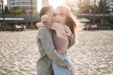 Happy couple of young people cuddle on the beach on the sunset. Beautiful sunlight. Casual clothes. Grunge style. High quality photoの写真素材