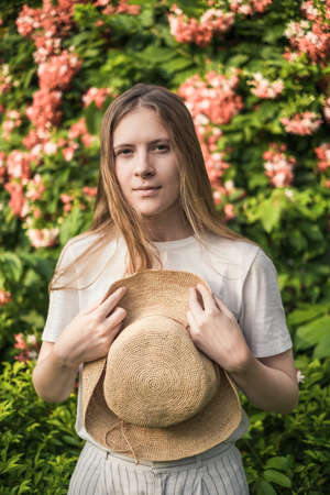 Portrait of lovely caucasian woman with long blond hair in the park. Holding straw hat in her hands....