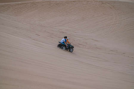 Picturesque view of ATV driving on sandy dunes and tire tracks on sand on sunny day during summer vacation. Two people driving ATV in white desertの写真素材