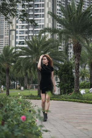 Beautiful young asian woman in casual black dress walking on the street with palm trees. Long hair....