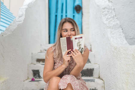 Portrait of pretty blond girl with attractive blue eyes in casual dress. Sitting outdoors with the book in front of her face. Mysterious lookの写真素材