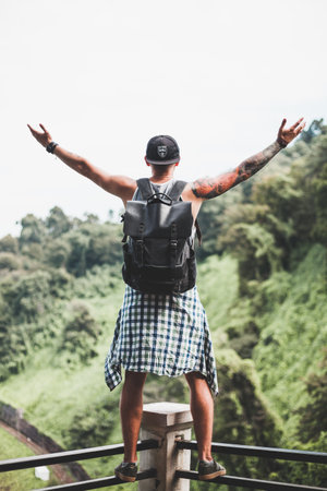 Guy with a tattoo all over his arm stands on the railing at the observation deck in the jungle....