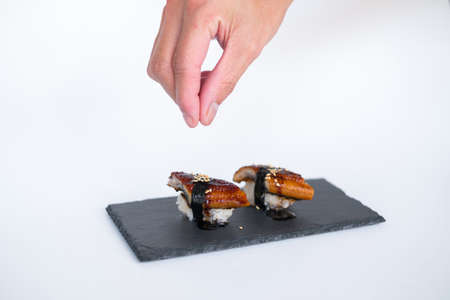 Japanese Sushi - Two Unagi Nigiri Sushi served on a black stone board. Eel Sushi. Isolated on white background. Hand decorates sushi with sauseの写真素材