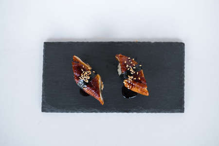 Japanese Sushi - Two Unagi Nigiri Sushi served on a black stone board. Eel Sushi. Sushi pieces served on black slate isolated on white background.の写真素材