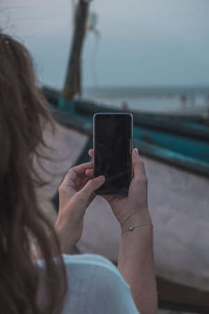 Over shoulder view: woman hands holding black mock up smartphone with blank screen. Mock up, copyspace, template, entertainment and technology conceptの写真素材