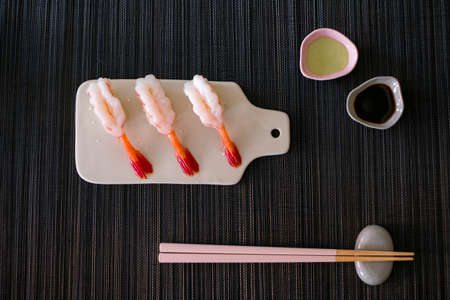 Raw Shrimp prawn sushi in japanese restaurant. Sushi - ama Ebi Nigiri on white board with chopsticks and souse on black background. High quality photoの写真素材