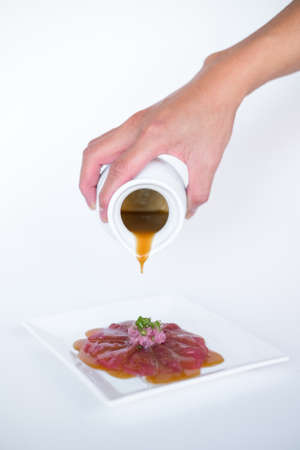 Hand pouring sauce on Tuna sashimi on white plate on white background. Isolated on white. The process of making and decorating tuna sashimi. Cookingの写真素材
