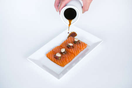 Hand pouring soy sauce on Salmon sashimi on white plate on white background. Isolated on white. Japanese traditional food. Healthy food concept.の写真素材
