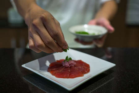 The chef prepares tuna sashimi. The process of making and decorating tuna sashimi. Tuna sashimi on white plate. Japanese traditional food.の写真素材