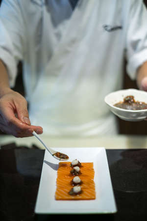 The chef prepares salmon sashimi. The process of making and decorating salmon sashimi. Salmon sashimi on white plate. Japanese traditional food.の写真素材